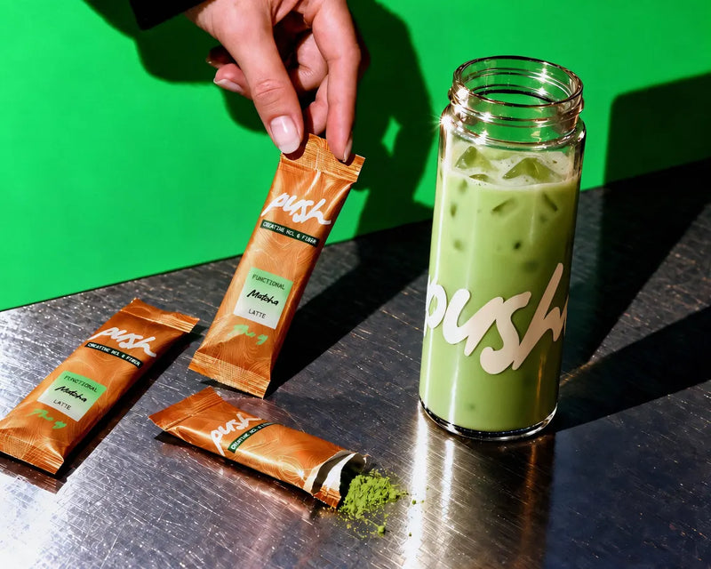 The Push tumbler of matcha latte and three sticks on brushed steel against lime