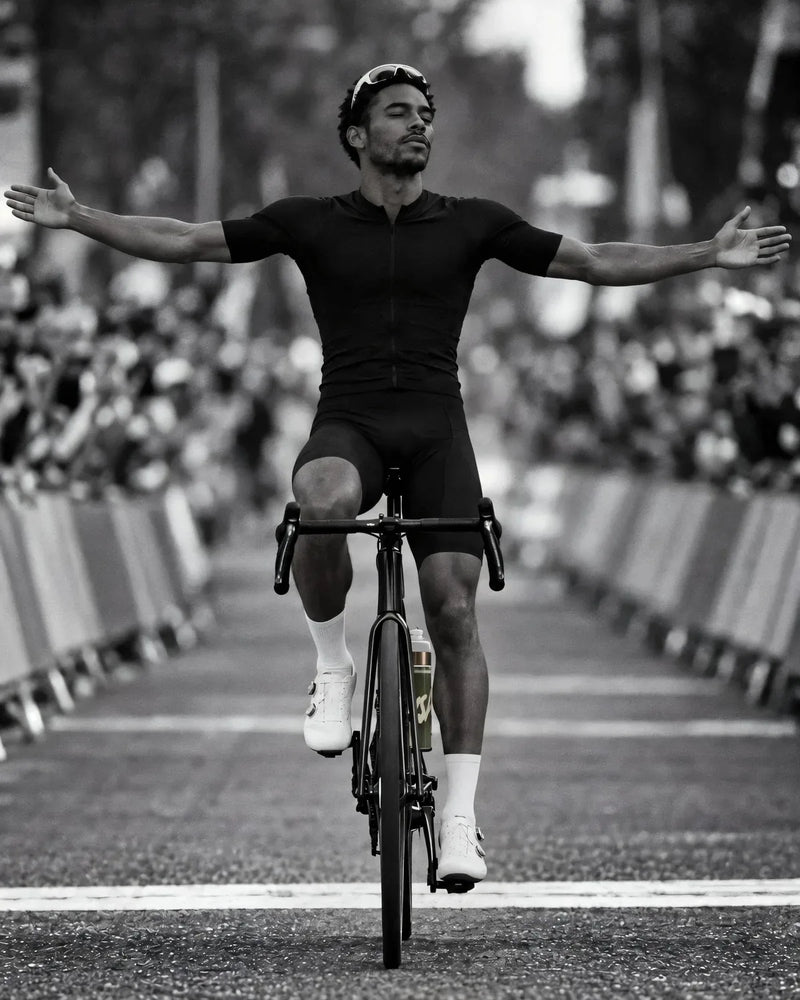 A cyclist crosses a finish line with both arms wide